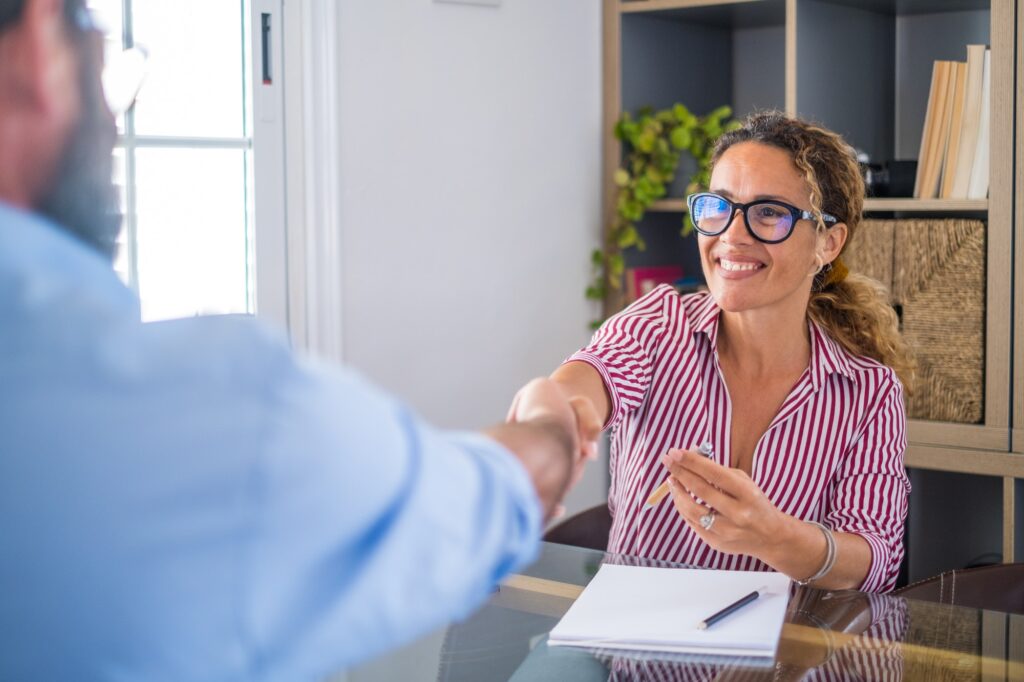 Smiling caucasian female hr manager handshake hire male candidate at job interview